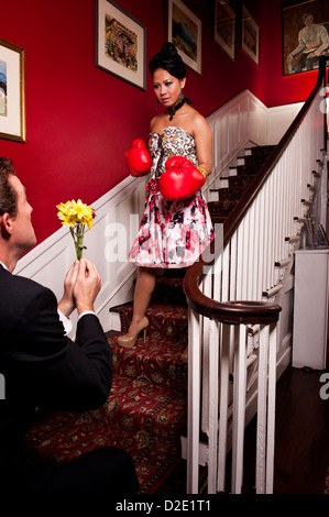 Homme ramenant des fleurs à la maison à une femme portant des gants de boxe impliquant de demander pardon à la femme en colère. Banque D'Images