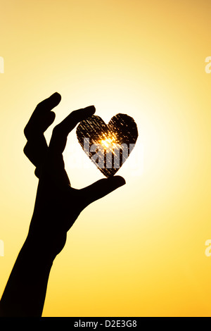 Les filles hand holding heart shape au coucher du soleil. Silhouette Banque D'Images