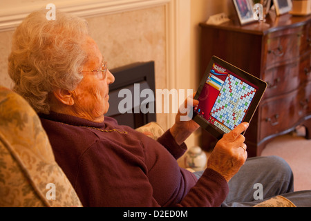 Femme âgée pensionné avec lunettes sur apple ipad tablet relaxing on président jouant un jeu informatique scrabble Banque D'Images