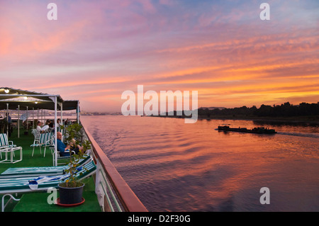 Avis de touristes de détente sur le pont supérieur d'un bateau de croisière au coucher du soleil sur le Nil au coucher du soleil l'Egypte Moyen Orient Banque D'Images