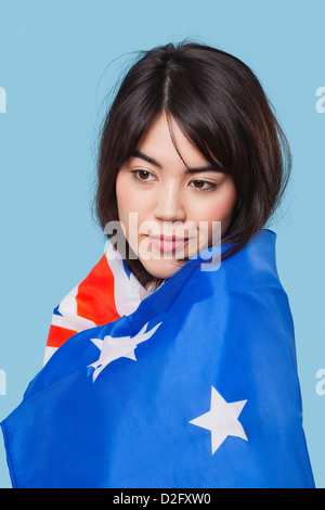 Jeune femme enveloppée dans patriotique drapeau australien sur fond bleu Banque D'Images