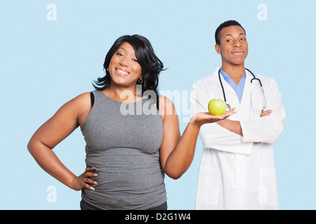 L'excès de mixed race woman holding green apple avec médecin sur fond bleu Banque D'Images