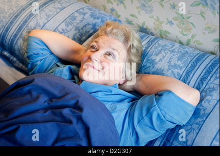 Retraite mature woman Lying in Bed smiling avec ses mains derrière la tête Banque D'Images