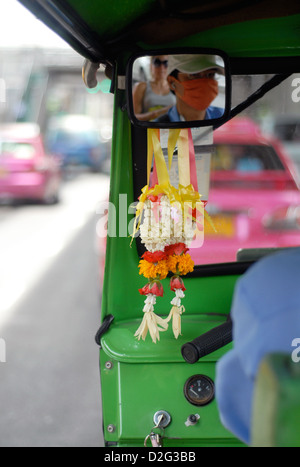 Des guirlandes de fleurs accrochées au rétroviseur de un tuk tuk reflétant le conducteur et passager à Bangkok en Thaïlande Banque D'Images