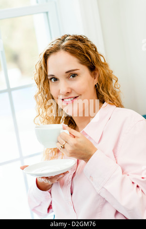 Smiling caucasian woman holding fenêtre par tasse de café Banque D'Images