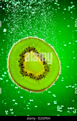 Kiwi frais tombe dans l'eau sur un fond vert Banque D'Images