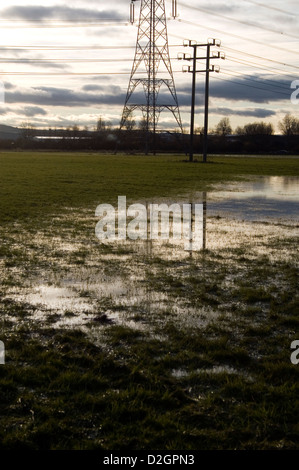 De grands pylônes reflétée dans un champ humide au Royaume-Uni. Banque D'Images