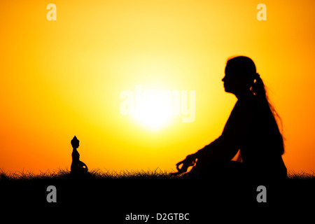 Sunset silhouette d'une jeune Indienne méditer en face de statue de Bouddha. L'Andhra Pradesh, Inde Banque D'Images