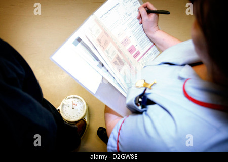 Patient debout sur un pèse-personne, tandis que le personnel infirmier et le poids de l'étude document dans Patient Notes Banque D'Images