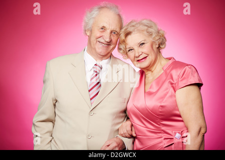 Portrait d'un charmant couple de retraités posant contre fond rose Banque D'Images