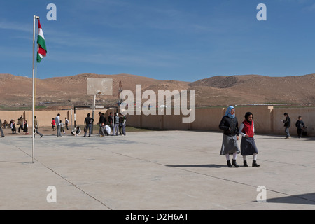 Les élèves de primaire et des jeux pour enfants à l'extérieur de l'école kurde irakienne dans le Nord de l'Iraq avec l'exploration pétrolière Rig derrière Banque D'Images