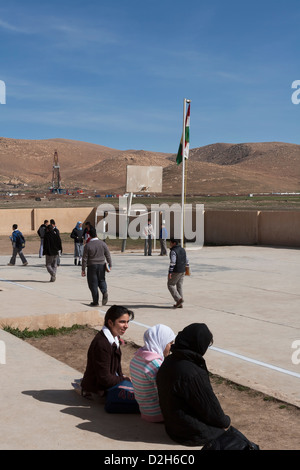 Les élèves de primaire et des jeux pour enfants à l'extérieur de l'école kurde irakienne dans le Nord de l'Iraq avec l'exploration pétrolière Rig derrière Banque D'Images