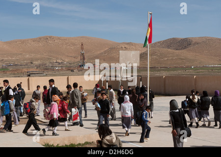 Les élèves de primaire et des jeux pour enfants à l'extérieur de l'école kurde irakienne dans le Nord de l'Iraq avec l'exploration pétrolière Rig derrière Banque D'Images