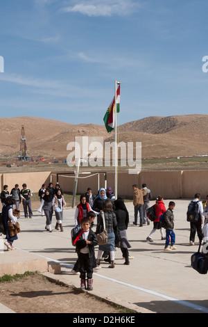 Les élèves de primaire et des jeux pour enfants à l'extérieur de l'école kurde irakienne dans le Nord de l'Iraq avec l'exploration pétrolière Rig derrière Banque D'Images