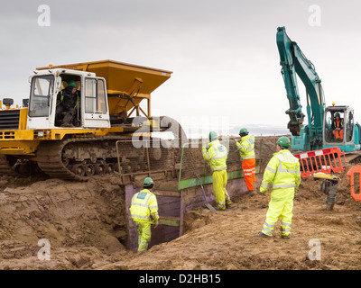 Ouvriers la pose d'une conduite d'égout de remplacement à l'aide d'un dumper à chenilles avec hopper et convoyeur pour remplir la tranchée Redcar Banque D'Images