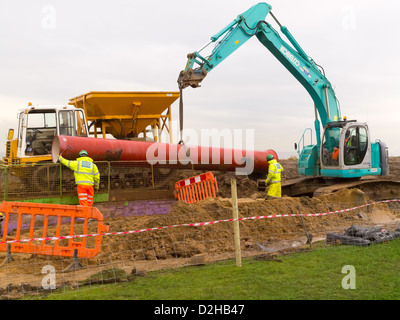 Ouvriers la pose d'une conduite d'égout de remplacement à l'aide d'une excavatrice pour soulever une nouvelle section de tuyau en place Redcar Banque D'Images