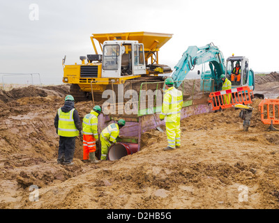 Ouvriers la pose d'une conduite d'égout de remplacement à l'aide d'une excavatrice pour soulever une nouvelle section de tuyau en place Redcar Banque D'Images