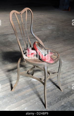 Vieux rouge chaussures usées sur rusty metal chaise avec plancher en bois sale pour un arrière-plan. Banque D'Images