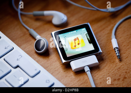 L'iPod nano avec un câble attaché, est assis sur un bureau à côté d'écouteurs Apple et le clavier d'un ordinateur. Banque D'Images