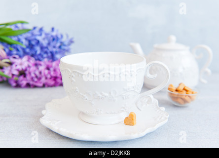 Tasse blanche et une théière avec un motif, vase avec des cookies en forme de coeur, des fleurs sur une table en bois Banque D'Images