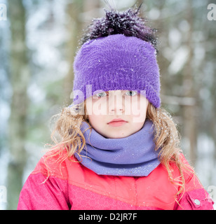 Petite fille blonde en hiver d'extérieur avec des flocons de neige au-dessus du fond de la forêt Banque D'Images