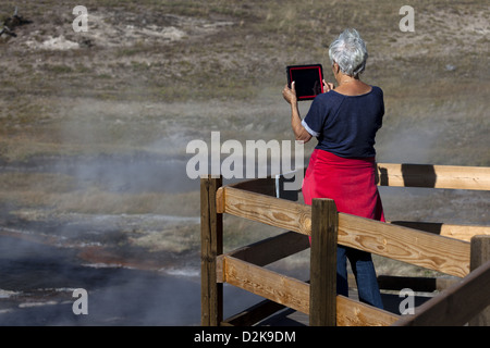 Femme âgée sur une passerelle en bois photographiant à Yellowstone, à l'aide d'une tablette iPad Banque D'Images