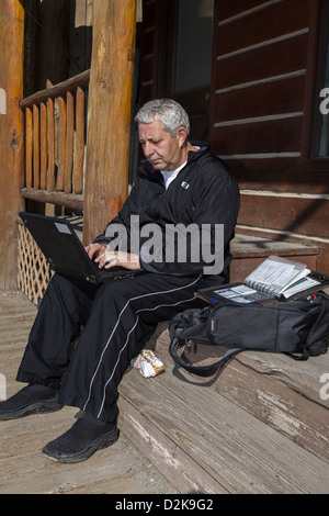 Homme assis sur une marche en bois en utilisant le hotspot local créant ainsi son propre bureau extérieur dans un ordinateur portable dans le centre-ville de Dubois, Wyoming États-Unis Banque D'Images