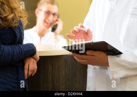 Le patient et le médecin dans l'espace réception de l'office de médecin ou dentiste, il est titulaire d'un presse-papiers, la réceptionniste est au téléphone Banque D'Images