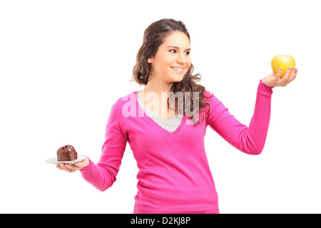 Douteux woman holding green apple et des gâteaux et en essayant de décider lequel de manger Banque D'Images