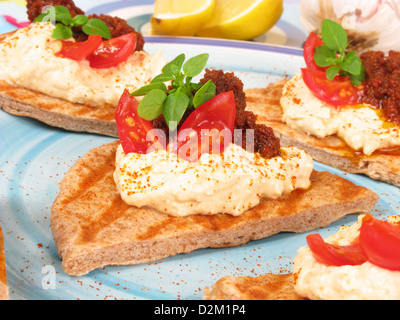 Un canape de style grec de griddled farine complète pain pita garni de l'hoummos, pesto de tomates, tomates et basilic frais. Banque D'Images