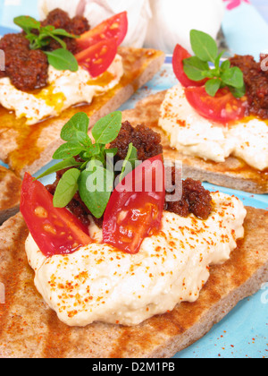 Un canape de style grec de griddled farine complète pain pita garni de l'hoummos, pesto de tomates, tomates et basilic frais. Banque D'Images