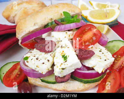 Un sandwich à la salade grecque : un rouleau de levain rempli de barils de fromage feta, olives Kalamata, oignons rouges, tomate et concombre. Banque D'Images