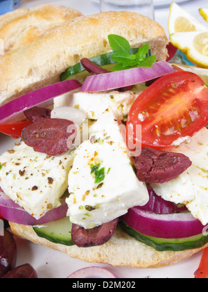 Un sandwich à la salade grecque : un rouleau de levain rempli de barils de fromage feta, olives Kalamata, oignons rouges, tomate et concombre. Banque D'Images