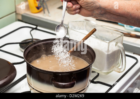 Détail de verser le sel dans la soupe bouillante en pot sur la cuisinière. Banque D'Images