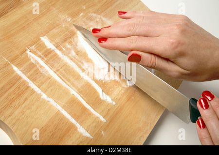 Une femme avec du vernis à ongles rouge préparer une ligne de cocaïne sur une planche à découper en bois. Banque D'Images