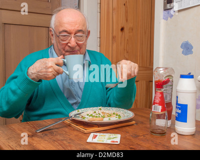 Un homme âgé assis à table à manger manger et boire Banque D'Images