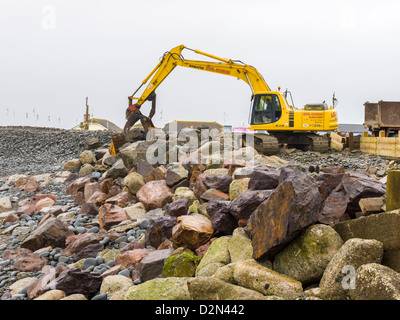 Un mechanical digger est utilisé pour effectuer l'entretien et la réparation de la défense de la mer sur la crête de galets à Westward Ho ! Plage. Devon, Angleterre. Banque D'Images