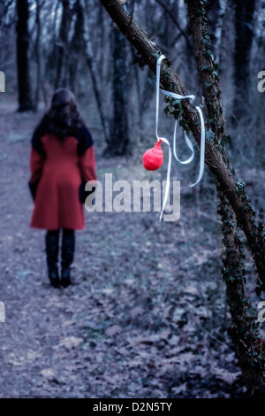 Un vieux ballon rouge suspendu à une branche, à une distance d'une femme dans un manteau rouge Banque D'Images