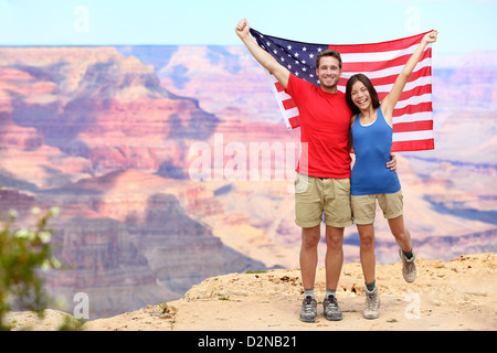 Happy young couple cheering multiethnique tout en maintenant drapeau américain à Grand Canyon South Rim lors des vacances d'été Banque D'Images