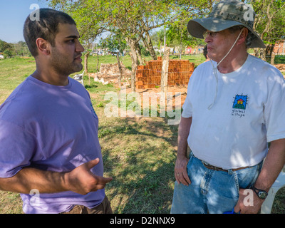 Un bénévole adulte parle avec un chef d'équipe d'Habitat pour l'humanité sur le site des travaux à Luque, Paraguay. Banque D'Images