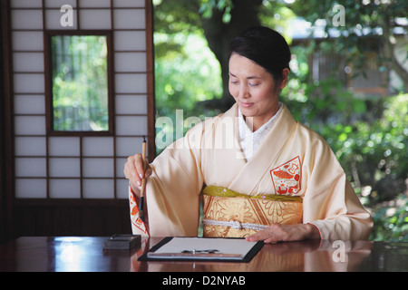 Femme dans un kimono pratiquer la calligraphie Banque D'Images