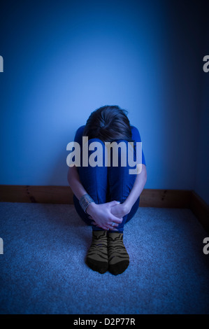 Teenage girl sitting appuyée contre un mur, la tête baissée entre ses genoux. Banque D'Images