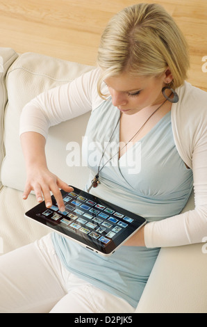 Hambourg, Allemagne, une jeune femme assise sur le canapé avec son iPad Banque D'Images