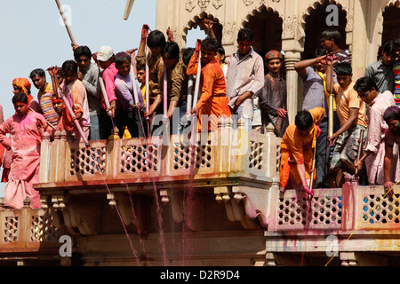 Les jeunes hommes célébrant Holi festival par éclaboussures fluides colorés sur les visiteurs du temple, Nandgaon, Uttar Pradesh, Inde, Asie Banque D'Images