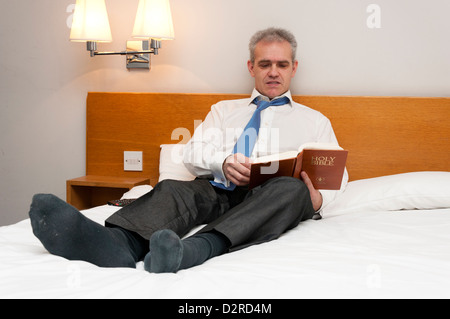 L'homme d'affaires en chambre d'hôtel reading Gideons Holy Bible Banque D'Images