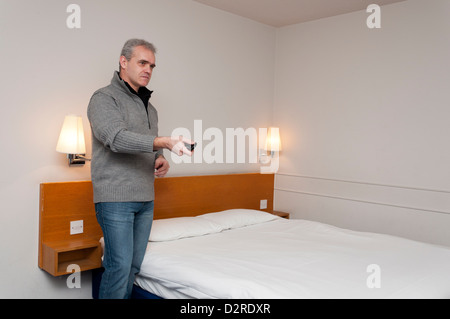 L'homme regardant la TV dans chambre d'hôtel, à l'aide de la télécommande. Banque D'Images