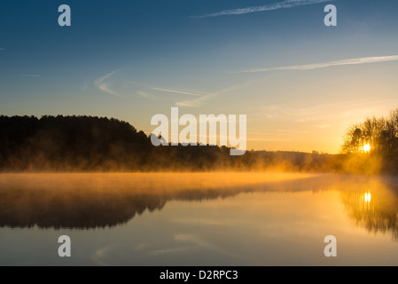 Le soleil n'est qu'à venir plus de West Point Lake, brillant à travers les arbres et se reflète sur l'eau. Ses rayons orange allume le brouillard tôt le matin. L'horizon est légèrement en dessous du centre de l'image en insistant sur le ciel. Banque D'Images