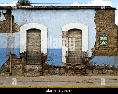 Façade sur rue abandonné adobe maison avec l'effritement du plâtre bleu et signe de la construction d'avertissement affichés en mauvais état Oaxaca Mexique Banque D'Images