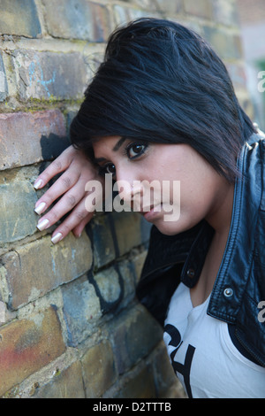 Bouleversé et effrayé Asian girl appuyé contre un mur de briques Banque D'Images