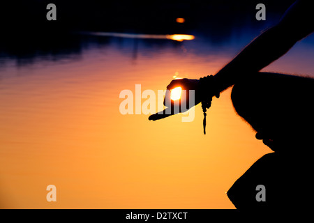 Silhouette d'un lever de mans la main, tout en méditant sur des pierres sur un lac. L'Andhra Pradesh, Inde Banque D'Images